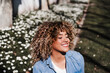 © Eva - smiling hispanic woman with eyes closed in park enjoying sunny day. Spring flowers background