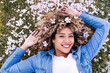 © Eva - portrait of happy hispanic woman with afro hair lying on grass among pink blossom flowers.Springtime