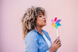© Eva - beautiful happy hispanic woman with afro hair holding colorful pinwheel. pink background,wind energy