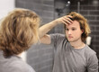 © lado2016 - young man looking in the mirror,combing his hair,looking at problems on face.