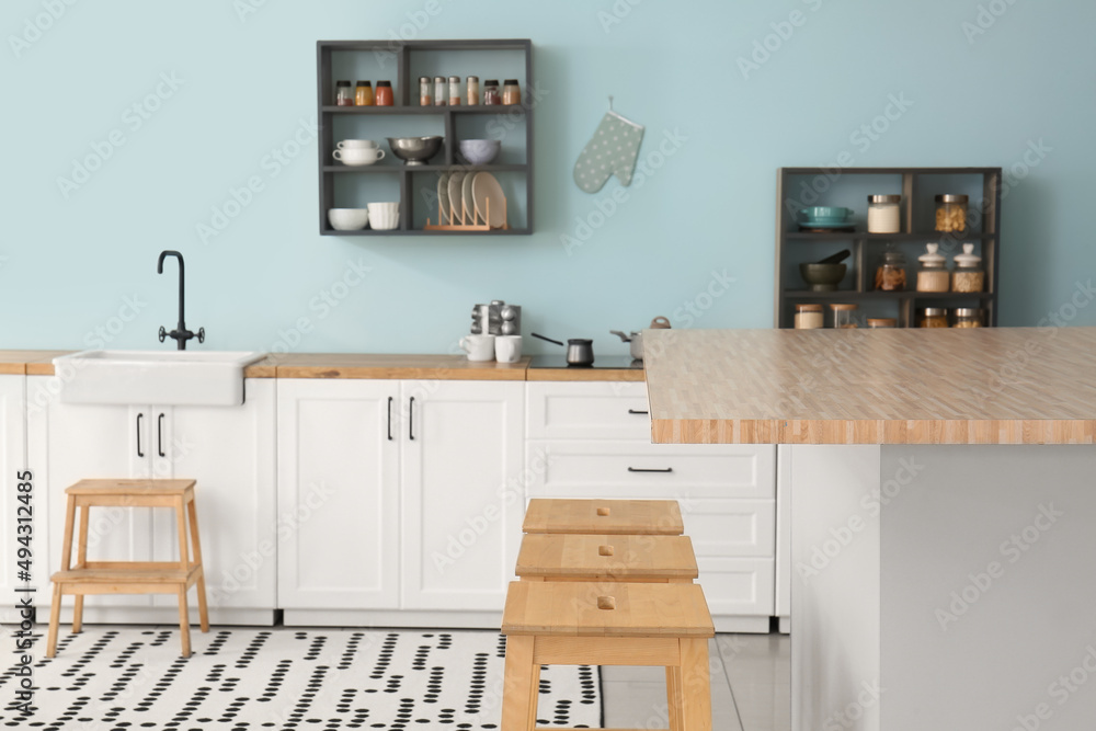 Interior of stylish kitchen with white counters, shelves and supplies