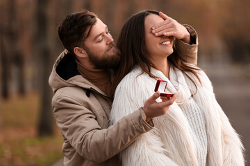 Wall Mural - Young man with engagement ring closing her girlfriend's eyes in park