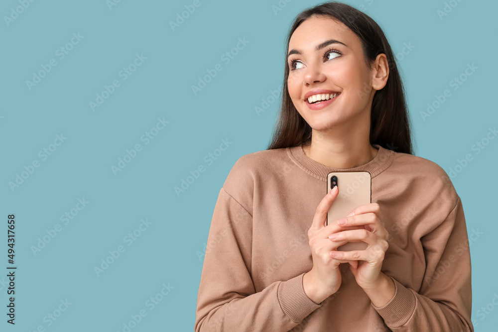 Beautiful young woman with mobile phone on blue background