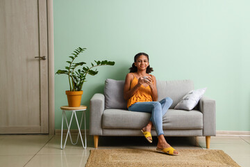 Sticker - African-American teenage girl drinking tea while sitting on sofa at home