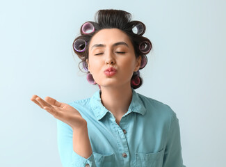 Wall Mural - Beautiful young woman in hair rollers blowing kiss on light background
