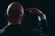 © mark_gusev - Bald business man in dark classic suit making hand gesture. Black background. Hands pointing to his head. Use your brain and think concept. Activate brain power theme