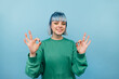 © bodnarphoto - Joyful hipster lady with colored hair with a smile on her face stands on a blue background and shows a gesture ok to the camera.