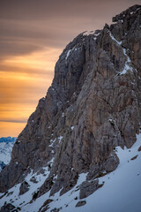 Poster - Vertical low angle shot of snowy mountain high in the winter with a orange-yellow blurred skyline