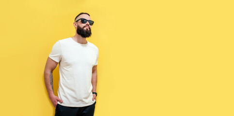 Wall Mural - Young bearded hipster guy wearing white blank t-shirt. Studio shot on yellow background. Mock-up for print. T-shirt template.