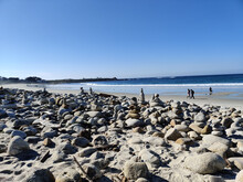 Sandy Beach With Stones And People Walking