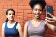 © etonastenka - Image of amazing young athletic women taking a selfie against a brick wall. Smiling black women spend time together after sports workout