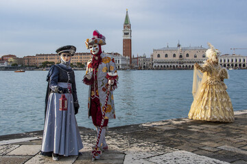 View of two women and a man in carnival clothing standing against a body of water in a harbor