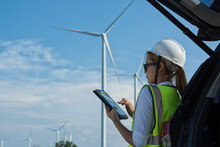 Service Engineers Woman Checking Tablet Against Cars On Wind Turbine Farm Background. Renewable Ennergy ,sustainable Concept. Wind Turbine Installation.