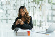 © PaeGAG - A beautiful Asian woman with smiley face holding and looking at smart phone while using laptop on wooden table in office