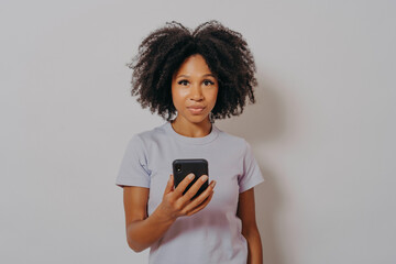 Wall Mural - Young african american female with curly hair using mobile phone and looking at camera