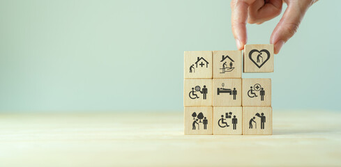 Wall Mural - Elderly care concept. Hand holds wooden cubes with icons related to elderly care, medical, rehabilitation service, nursing care for enhancing quality of life in elder age. Used for banner, background.