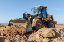 Bulldozer Or Loader Moves The Earth At The Construction Site Against The Blue Sky. An Earthmoving Machine Is Leveling The Site. Construction Heavy Equipment For Earthworks.