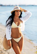 © Syda Productions - people, summer holidays and leisure concept - happy woman in bikini swimsuit, white shirt and straw hat with bag walking along beach