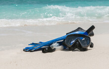 Mask And Fins For Scuba Diving And Snorkeling Lie On The Sandy Shore Against The Backdrop Of The Sea And Ocean.