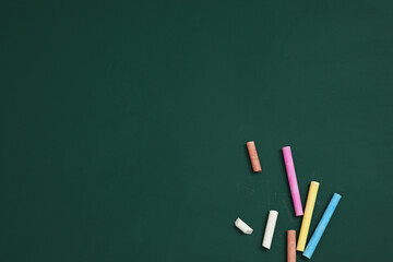 Wall Mural - Colorful chalks on green board, flat lay. Space for text