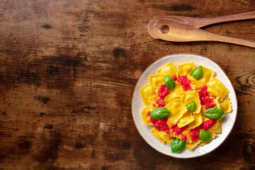 Wall Mural - Ravioli with red tomato sauce and basil, overhead flat lay shot with copy space. Vegan Italian cuisine, on a rustic wooden background