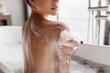 Home spa, hygiene concept. Young lady taking bath and rubbing her skin with sponge, relaxing in bathroom, closeup