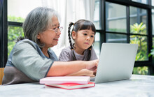 Asian Grandmother With Her Two Grandchildren Having Fun And Playing Education Games Online With A Computer Notebook At Home In The Living Room. Concept Of Online Education And Caring From Parents.