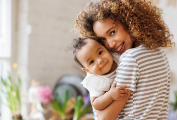 Happy, cheerful ethnic mom holds a laughing baby daughter in her arms