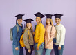 © Studio Romantic - Diverse group of happy cheerful successful university students with backpacks, in casual wear and square academic graduate hats standing against purple studio background, looking at camera and smiling