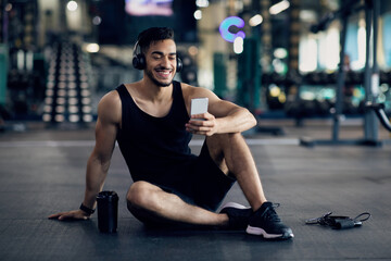 Wall Mural - Workout App. Happy Arab Male Athlete Using Smartphone After Training In Gym