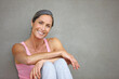 Living a healthy lifestyle. Portrait of an attractive mature woman in gymwear sitting against a gray wall.