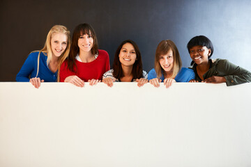 Poster - Place your message here. Shot of a group of women holding a blank sign against a dark background.