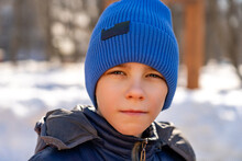 Portrait Of Confident Teen Boy In Winter In Warm Coat And Blue Hat Looks Directly Into Camera.