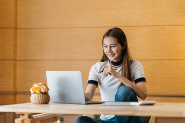 Wall Mural - Young happy Asian businesswoman sitting in front of laptop computer and smiling.