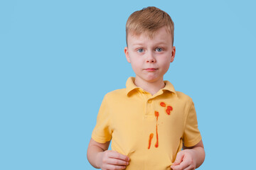 Sad boy showing spilled tomato sauce on his clothing. isolated on blue background