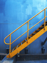 Vertical Shot Of A Yellow Metal External Staircase On A Blue Wall Background