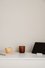 Wall Mural - Minimalist home office desk table. Feminine workspace with mug of tea, digital tablet, candle, paper notebooks. White wall background. Nordic, boho style living room interior.