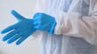 © ShantiMedia - A doctor puts on gloves before working in a covid hospital with infected patients. A health worker in a protective suit puts on blue latex gloves, carefully protects exposed skin. Coronovirus concept