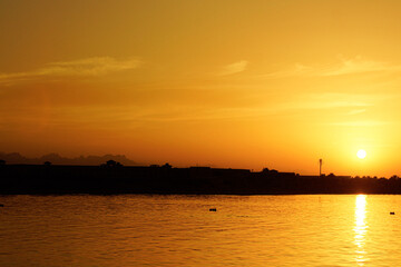 Canvas Print - Stunning view of bright sun and orange cloudless sunset sky reflected on a tranquil sea