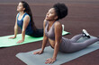 © etonastenka - Group yoga session of two beautiful multiethnic women outdoors. Women stood in the pose of a dog face up. Urdhva Mukha Svanasana