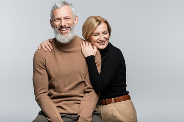 Blonde woman in turtleneck hugging mature husband isolated on grey.