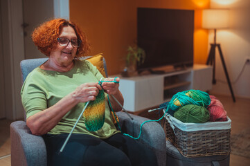 mature woman holding knitting needles and knitting at home.