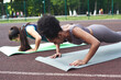 © etonastenka - Two athletic female friends do push-ups on the exercise mat at the stadium in the park. Muscle load.