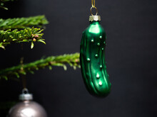 Christmas Tree Decorations. A Green Glass Cucumber Is Hanging On A Christmas Tree. Green Branches And A Black Background Are Visible.

