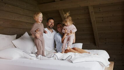 Wall Mural - Happy young family with small children having fun in bed on holiday.