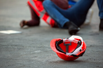 Red hard safety helmet hat for engineer on concrete ground with African-American male engineers injured the accident from working  blurred image background.