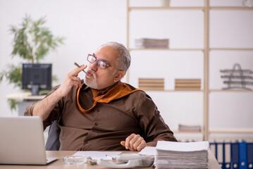 Old male employee smoking cigarette at workplace