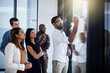 © Thurstan H/peopleimages.com - Hes showing them a new way of doing things. Shot of a young businessman giving a demonstration on a glass wall to his colleagues in a modern office.