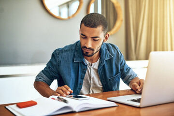 Poster - Crunching the numbers. Shot of a focused young man working on his laptop and checking his phone while being seated at a table at home.