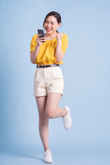 Wall Mural - Full length image of young Asian woman using smartphone on blue background